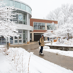 A student skateboards in beautiful winter scenery.