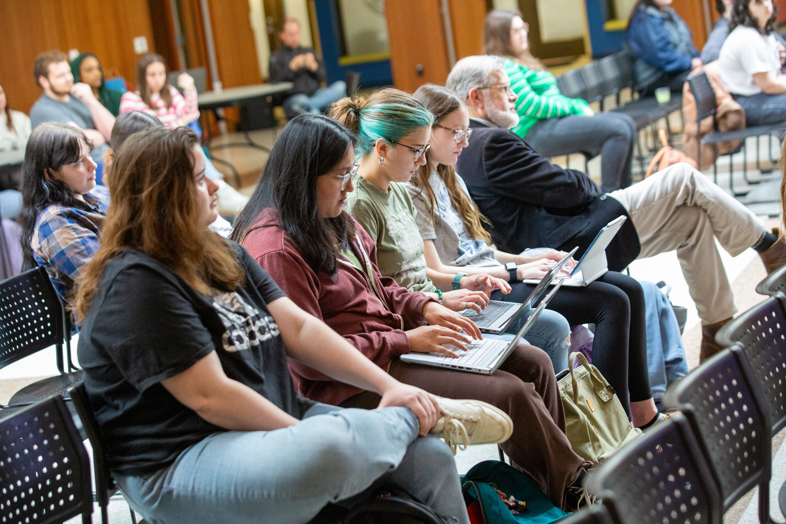 A group of mostly students listens to a speaker and takes notes.