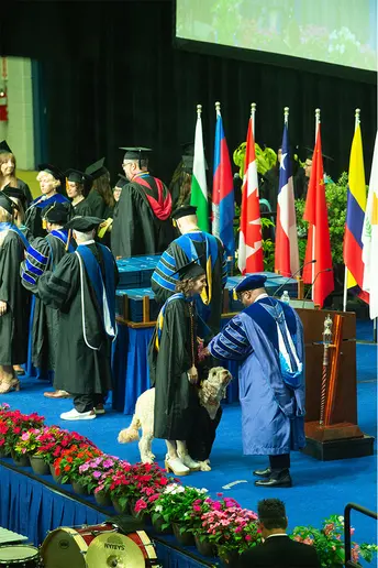 Madison Evans is escorted by her service dog, Sunny, as she prepares to shake hands with President Stephen H. Kolison Jr.